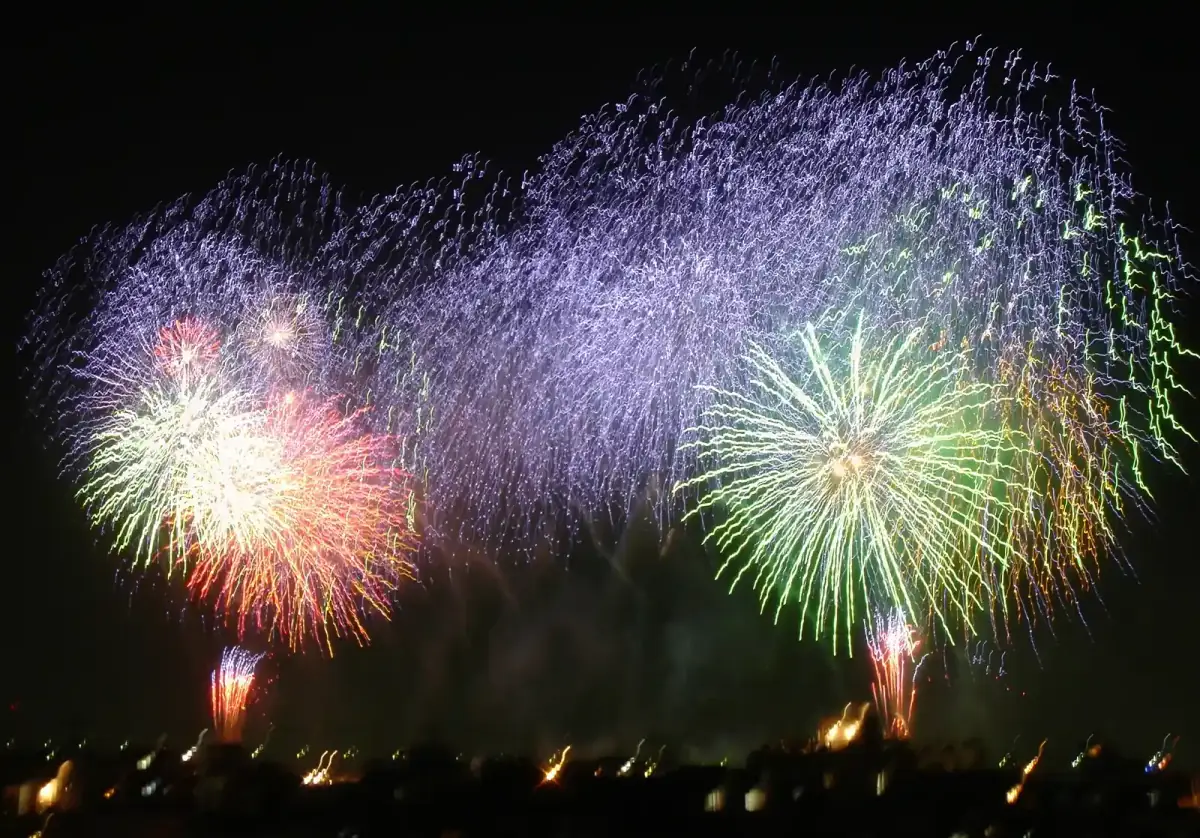 Colorful summer fireworks bursting over a river and city in July