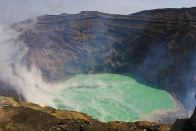 The turquoise crater lake at Mount Aso's active Nakadake crater, ringed by steam and volcanic rock